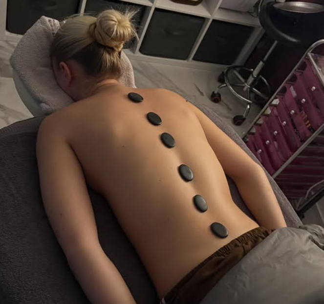 Smooth black hot stones positioned along the spine of a person receiving a hot stone massage in a spa setting. at Beauty by Bex