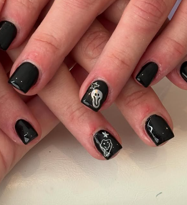 SClose-up of hands with short black-painted nails, featuring small white ghost designs and star details on two accent nails.